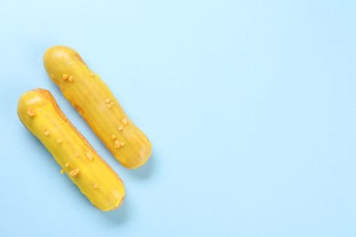 Photo of Delicious eclairs covered with glaze on light blue background, top view. Space for text