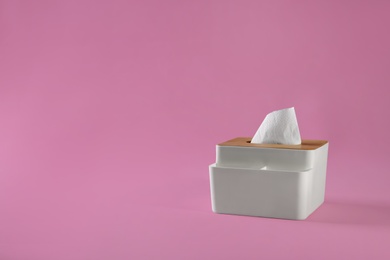 Photo of Holder with paper tissues on pink background. Space for text