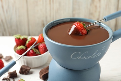 Photo of Dipping strawberry into fondue pot with chocolate, closeup