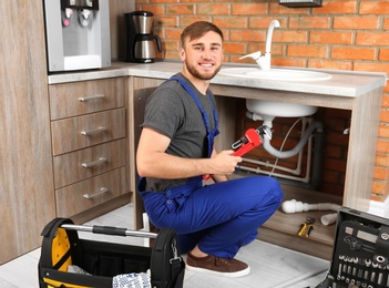 Photo of Professional plumber in uniform with pipe wrench near kitchen sink