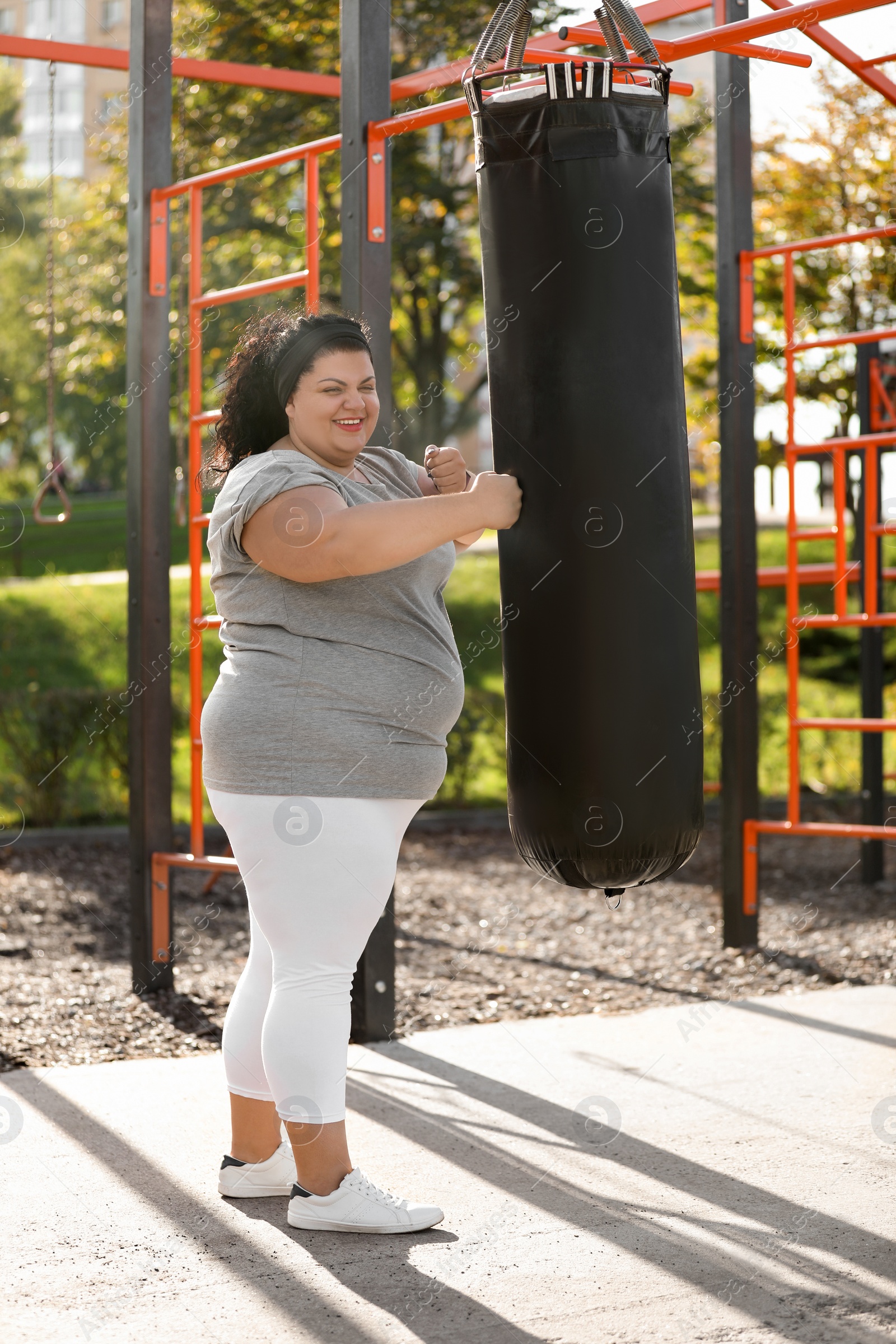 Photo of Beautiful overweight woman kicking heavy bag on sports ground