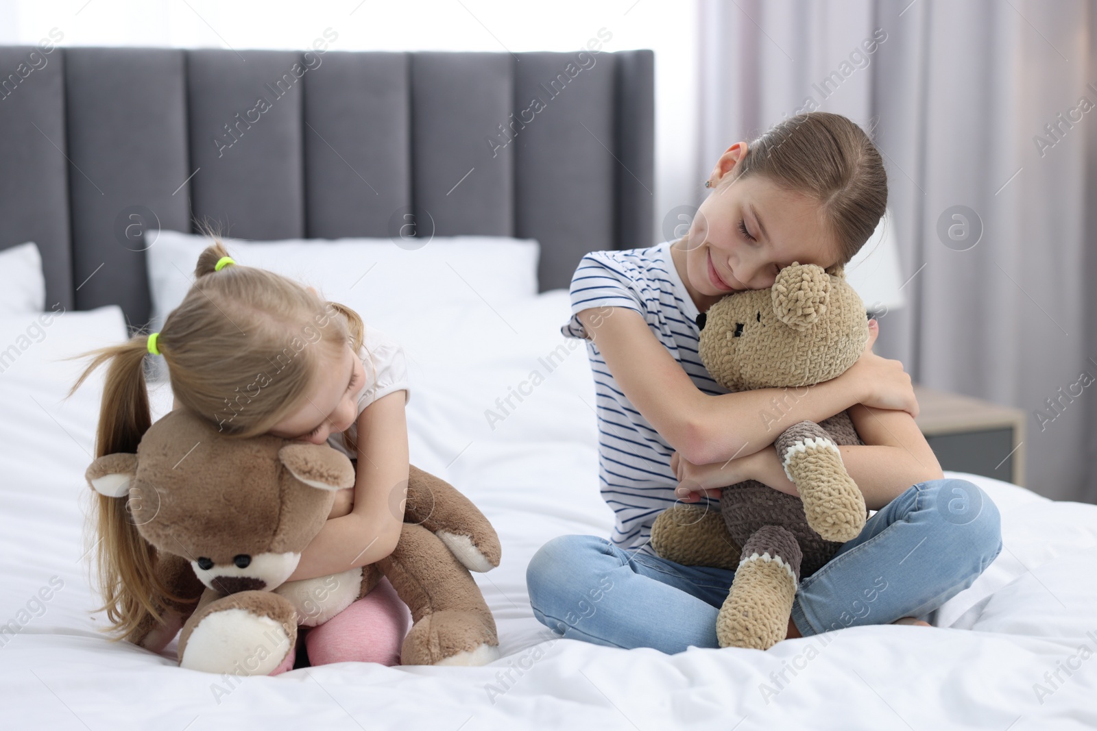 Photo of Cute little sisters with teddy bears on bed at home