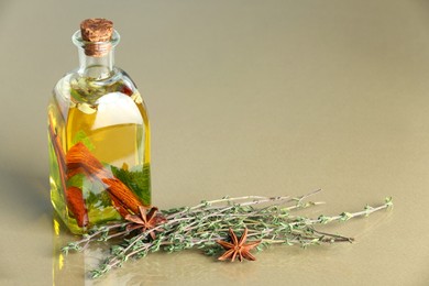 Photo of Cooking oil with spices and herbs in bottle on beige table. Space for text