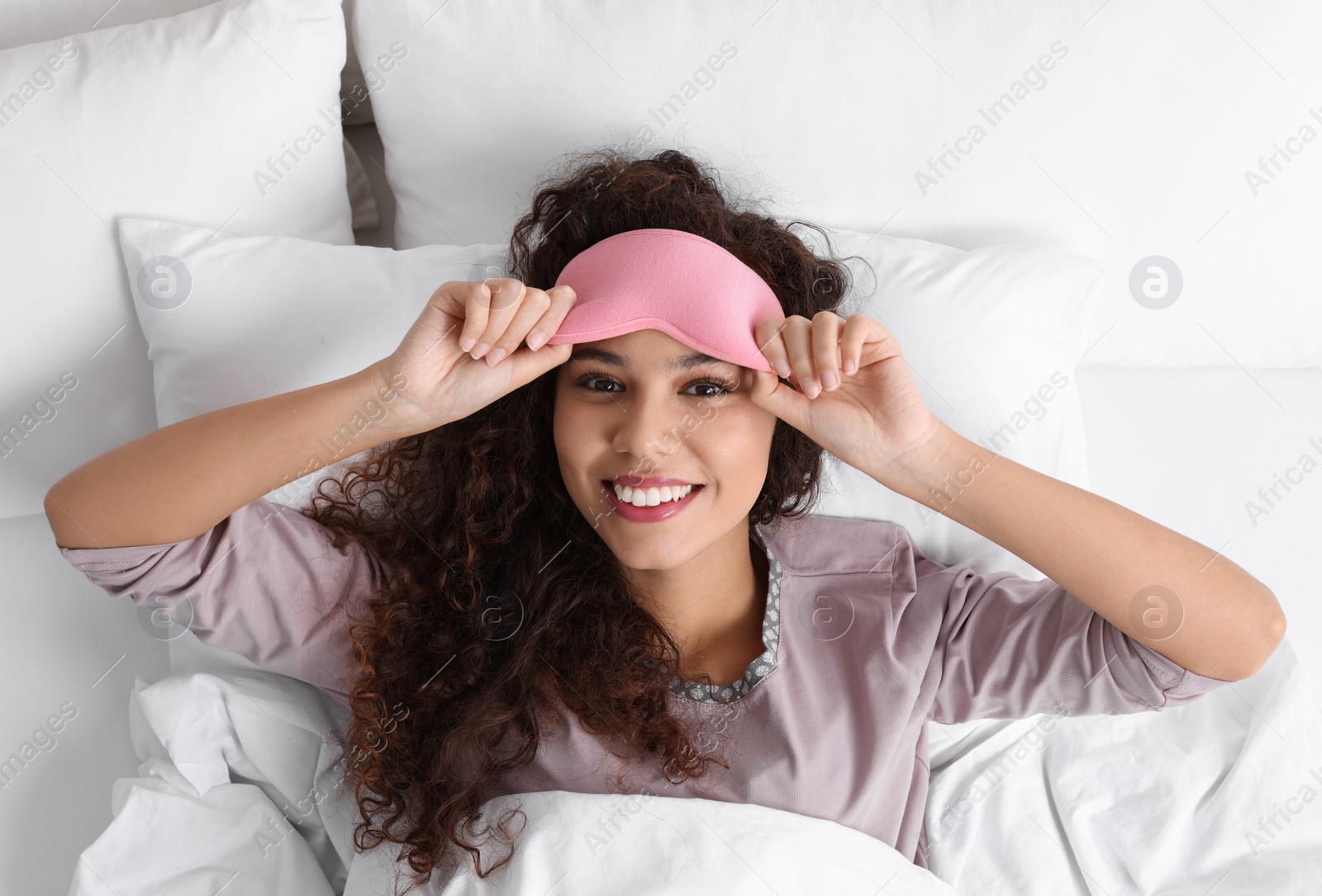 Photo of Happy African American woman with sleeping mask in bed, top view