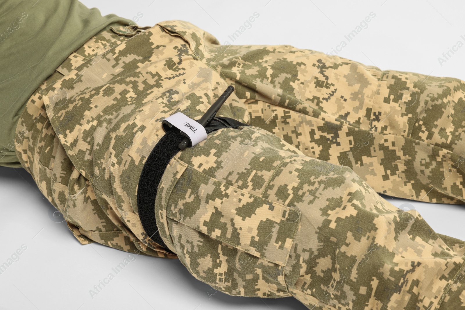 Photo of Soldier in military uniform with medical tourniquet on leg against white background, closeup