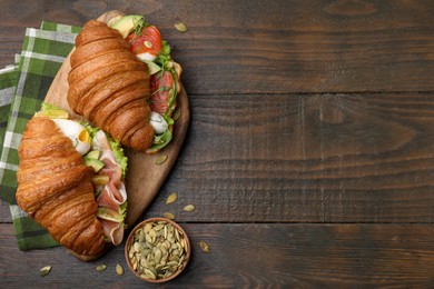 Delicious croissants with salmon, prosciutto and pumpkin seeds on wooden table, flat lay. Space for text