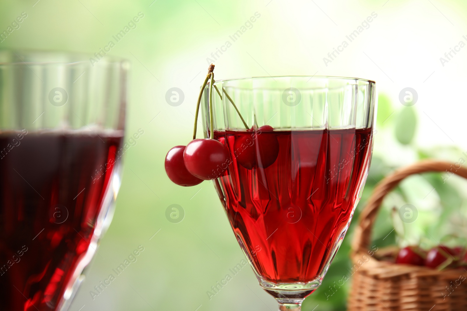 Photo of Delicious cherry wine with ripe juicy berries on blurred green background, closeup