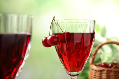 Photo of Delicious cherry wine with ripe juicy berries on blurred green background, closeup