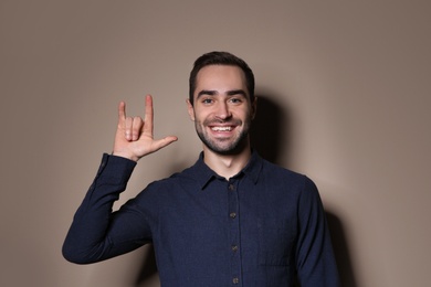 Photo of Man showing I LOVE YOU gesture in sign language on color background