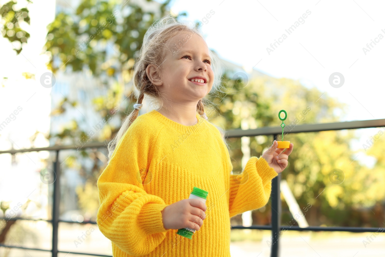 Photo of Cute little girl blowing soap bubbles outdoors