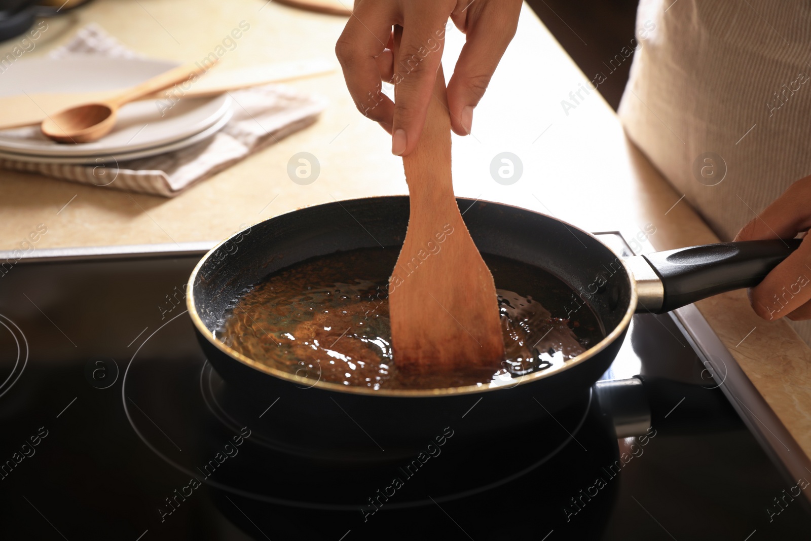 Photo of Woman with wooden spatula and frying pan of used cooking oil near stove, closeup