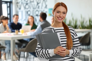 Photo of Team of employees working together in office. Happy woman with folders indoors, space for text