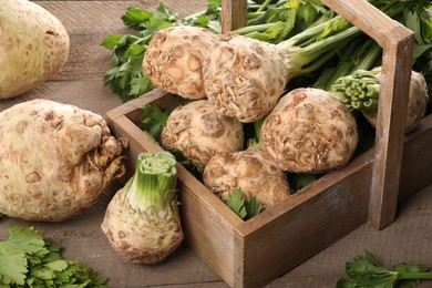 Photo of Fresh raw celery roots and crate on wooden table