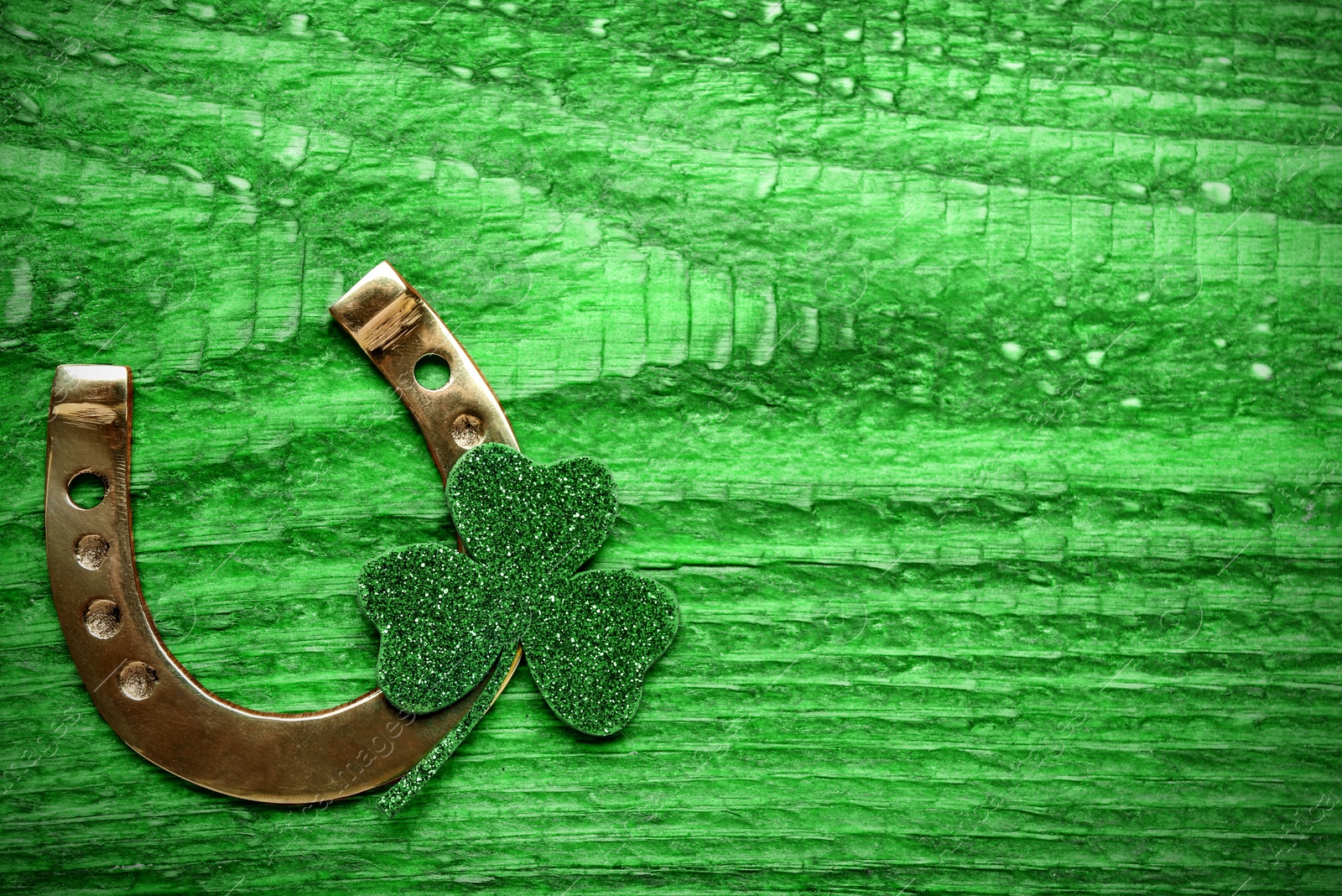 Image of Golden horseshoe and decorative clover leaf on green wooden table, flat lay with space for text. Saint Patrick's Day celebration