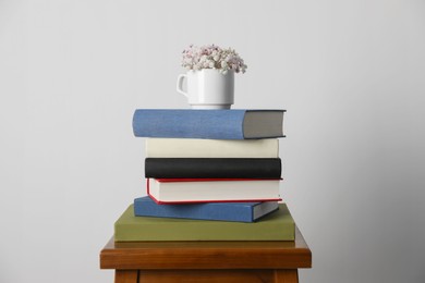 Photo of Hardcover books and cup with flowers on wooden stool near white wall