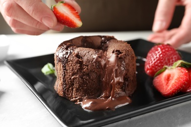 Chef decorating delicious fresh chocolate fondant with strawberry at table. Lava cake recipe