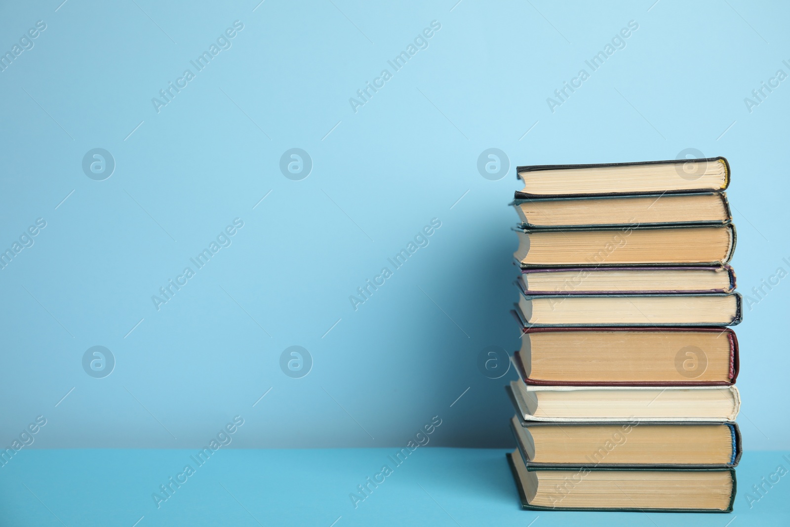 Photo of Stack of hardcover books on light blue background, space for text