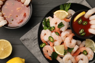 Tasty boiled shrimps with cocktail sauce, chili, parsley and lemon on grey wooden table, flat lay