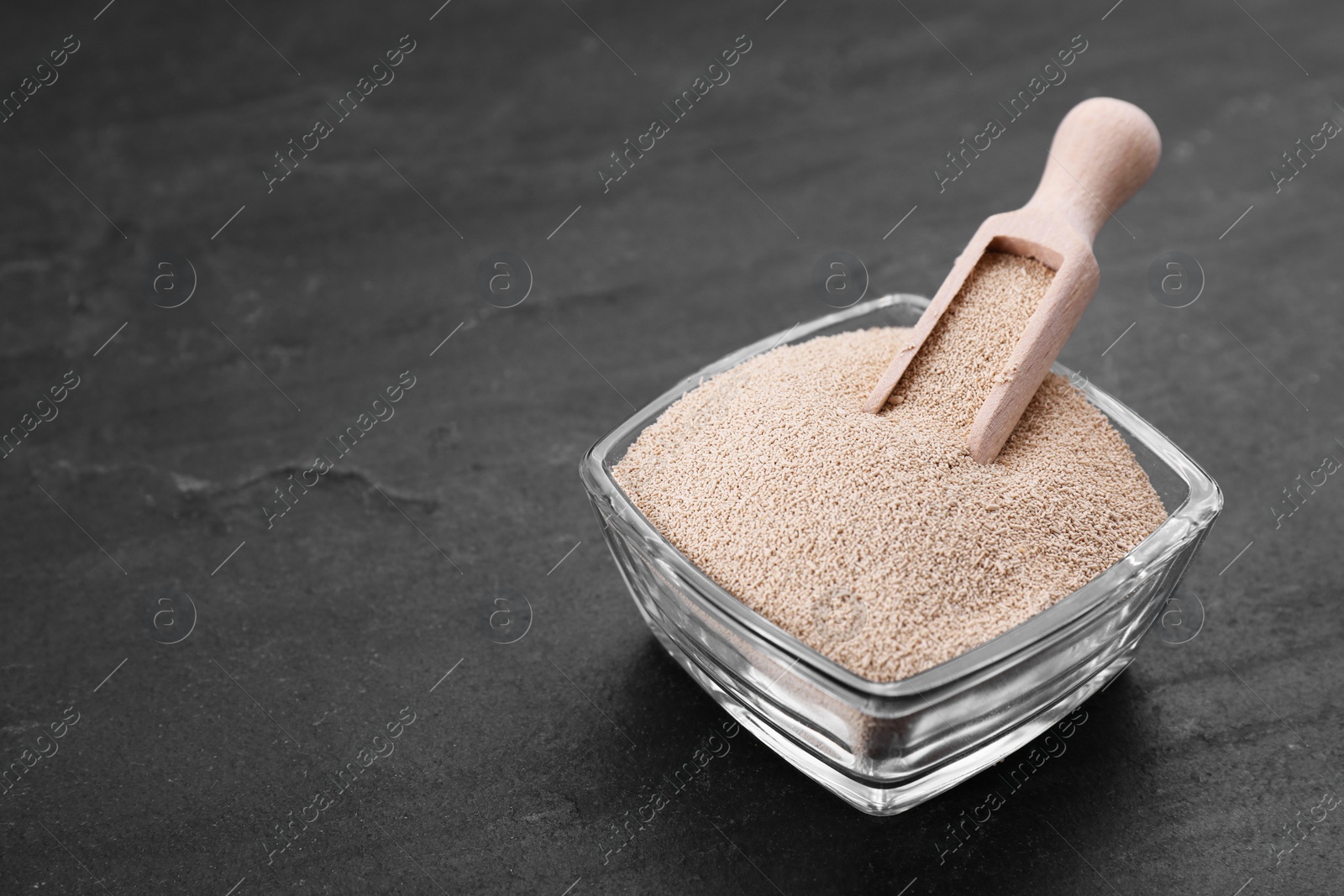 Photo of Bowl and scoop with active dry yeast on black table, closeup. Space for text