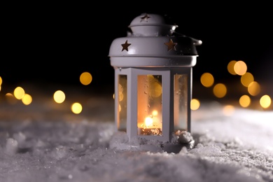 Photo of Lantern with burning candle and Christmas lights on white snow outdoors. Space for text