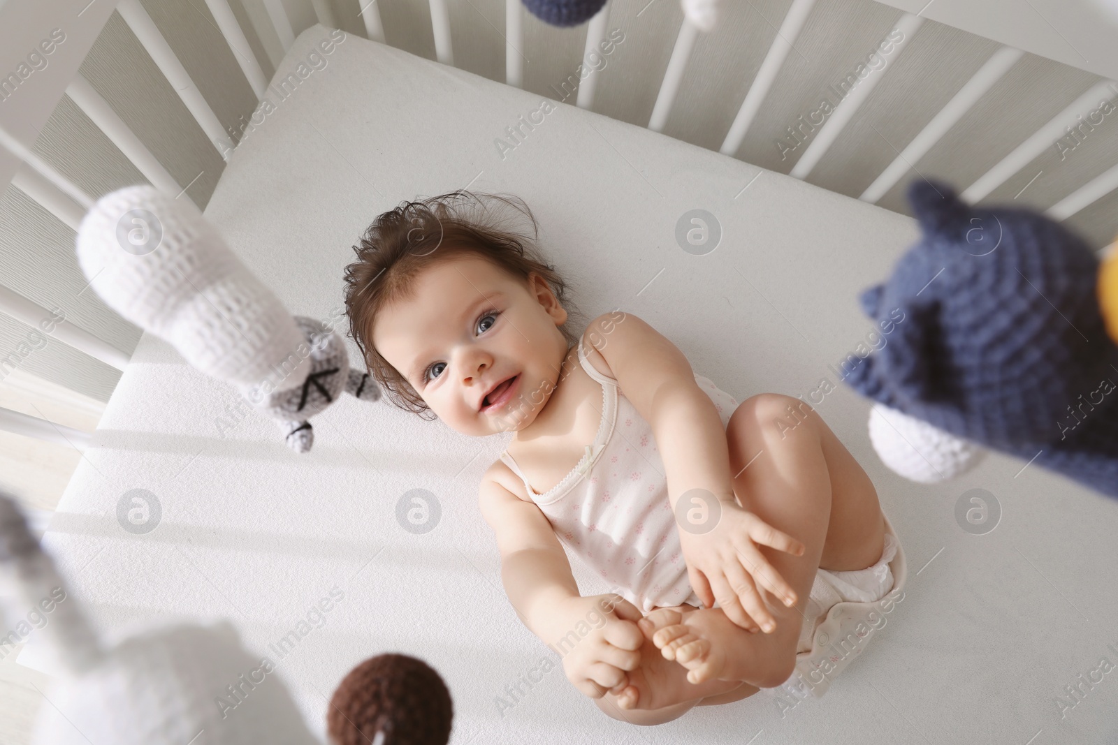 Photo of Cute little baby looking at hanging mobile in crib, top view