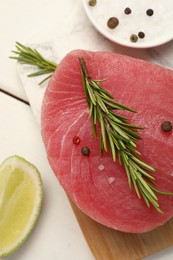 Raw tuna fillet with rosemary and spices on white table, top view