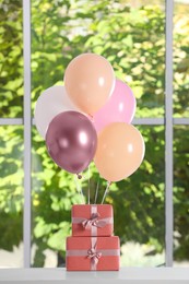 Bunch of color balloons and beautifully wrapped gift boxes on white table near window