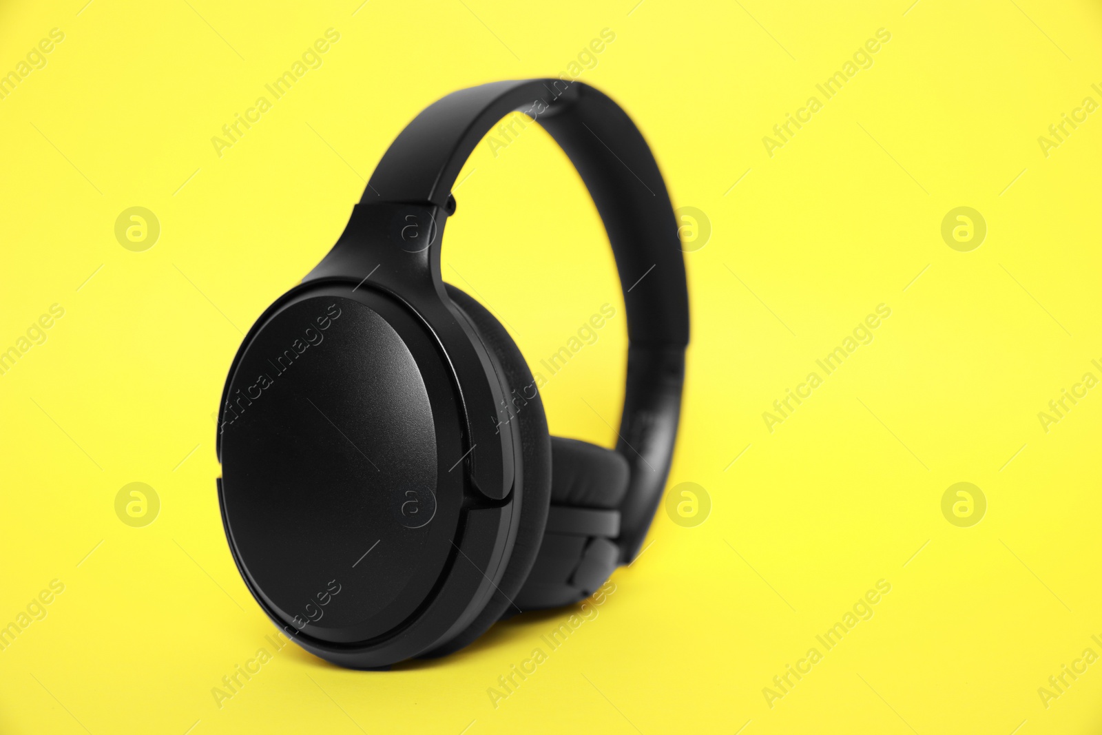 Photo of Modern black wireless headphones on yellow background, space for text