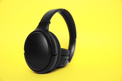 Modern black wireless headphones on yellow background, space for text