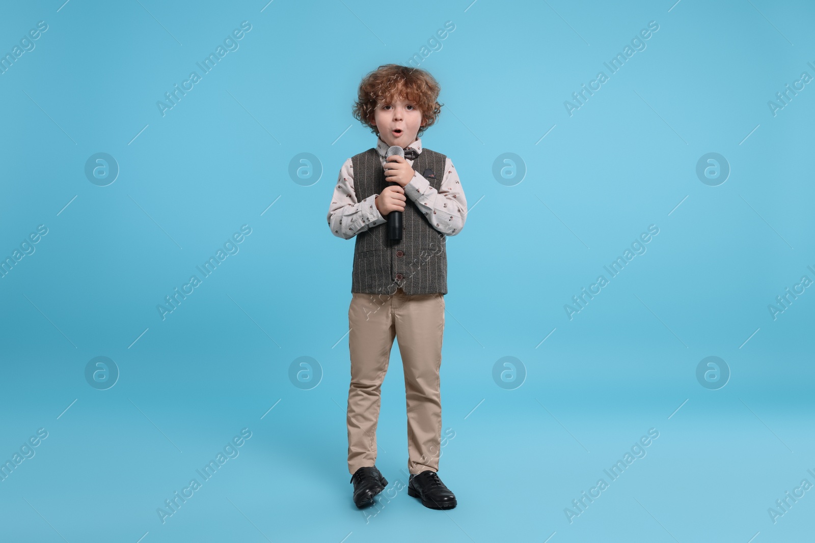 Photo of Cute little boy with microphone singing on light blue background