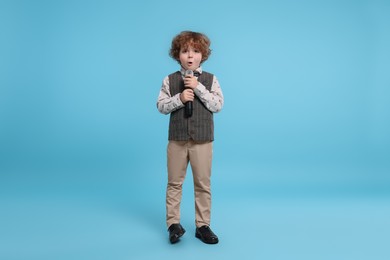 Cute little boy with microphone singing on light blue background