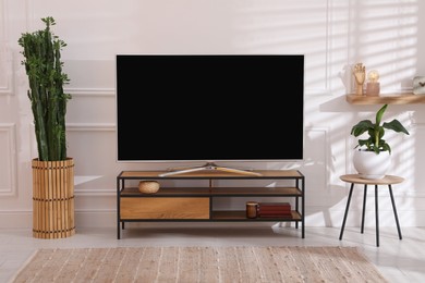 Modern TV on stand near white wall indoors. Interior design