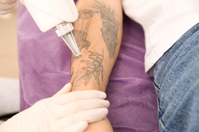 Young man undergoing laser tattoo removal procedure in salon, closeup