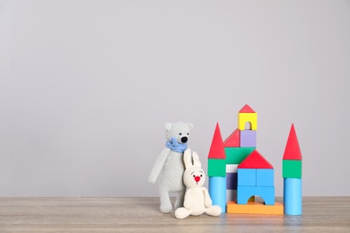Photo of Cute toys and castle made of colorful blocks on table against light background, space for text. Child room elements
