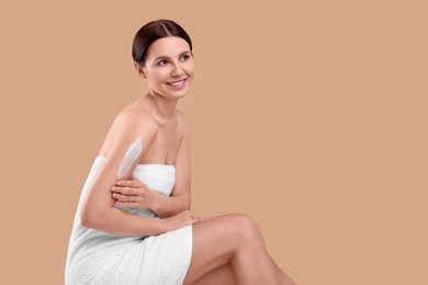 Photo of Beautiful woman with smear of body cream on her arm against light brown background, space for text