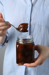 Photo of Woman holding jar of tasty sweet fig jam on grey background, closeup