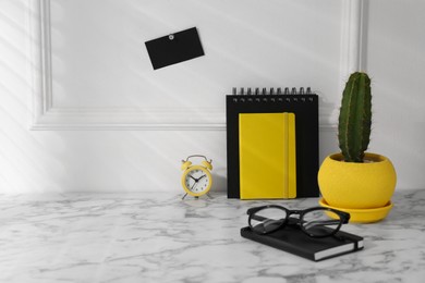 Photo of Stylish office workplace. Decor elements, cactus, glasses and stationery on marble table near white wall. Space for text