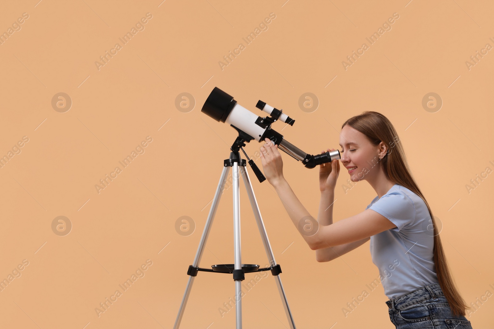 Photo of Young astronomer looking at stars through telescope on beige background, space for text