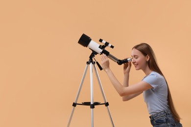 Young astronomer looking at stars through telescope on beige background, space for text