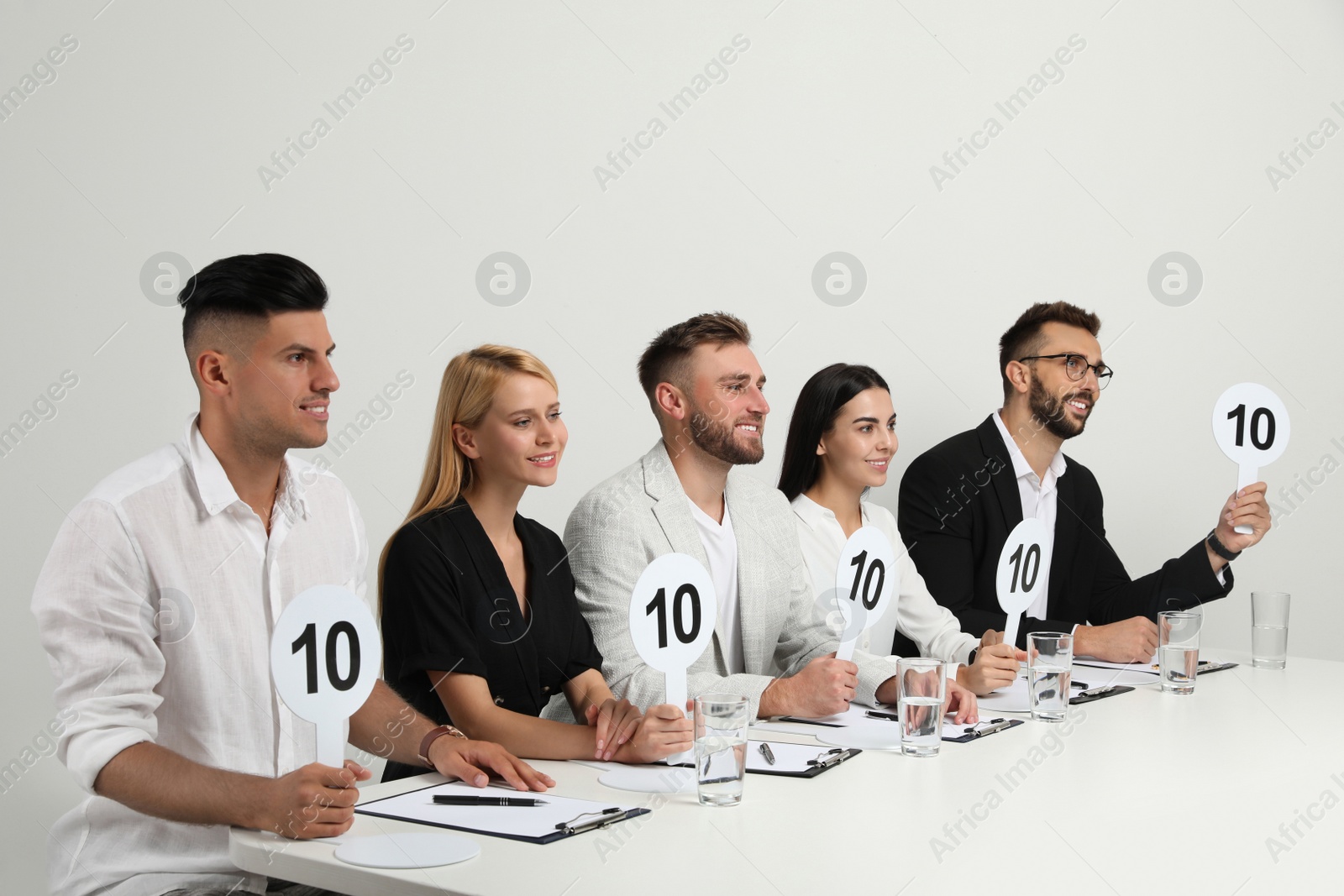 Photo of Panel of judges holding signs with highest score at table on white background