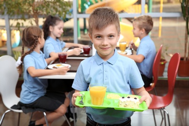 Photo of Cute boy holding tray with healthy food in school canteen