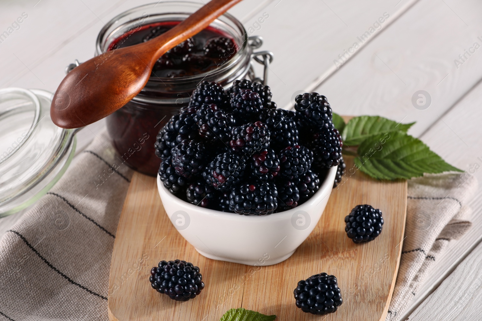 Photo of Fresh ripe blackberries, tasty jam and leaves on white wooden table