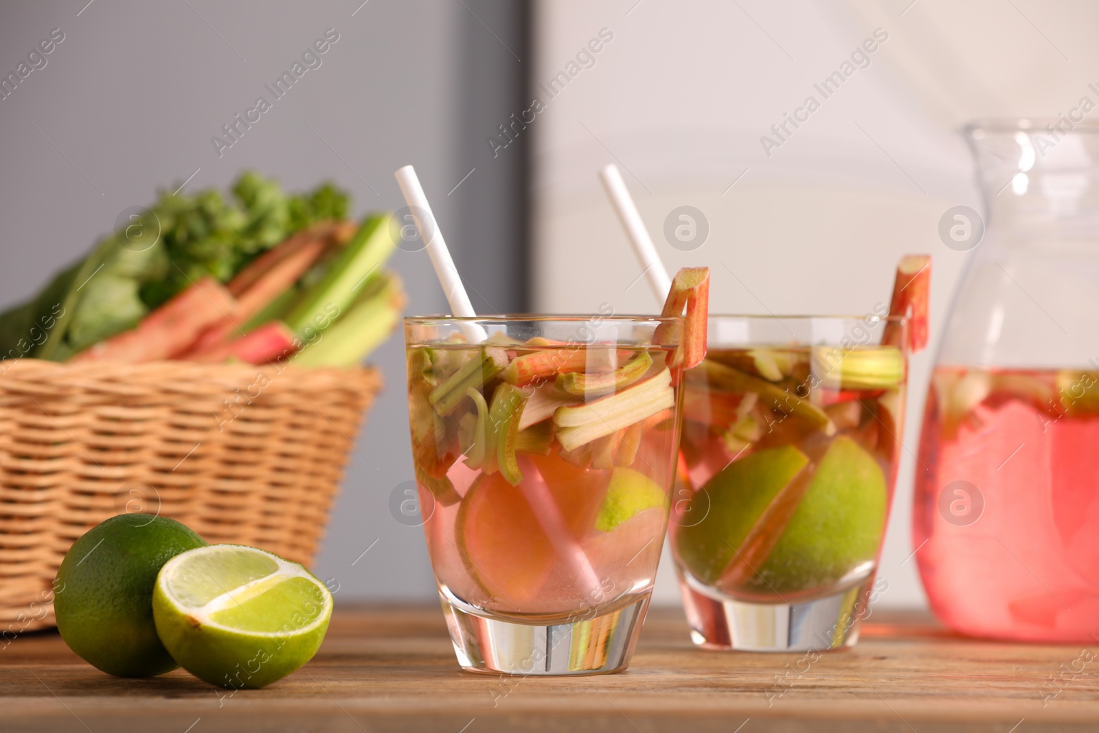 Photo of Glasses and jug of tasty rhubarb cocktail with lime fruits on wooden table