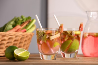 Glasses and jug of tasty rhubarb cocktail with lime fruits on wooden table