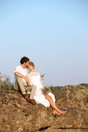 Happy newlyweds with beautiful field bouquet sitting on rock outdoors