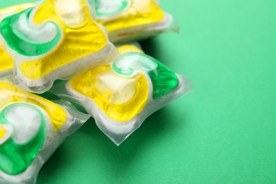 Photo of Many dishwasher detergent pods on green background, closeup. Space for text