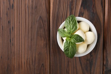 Tasty mozarella balls and basil leaves in bowl on wooden table, top view. Space for text