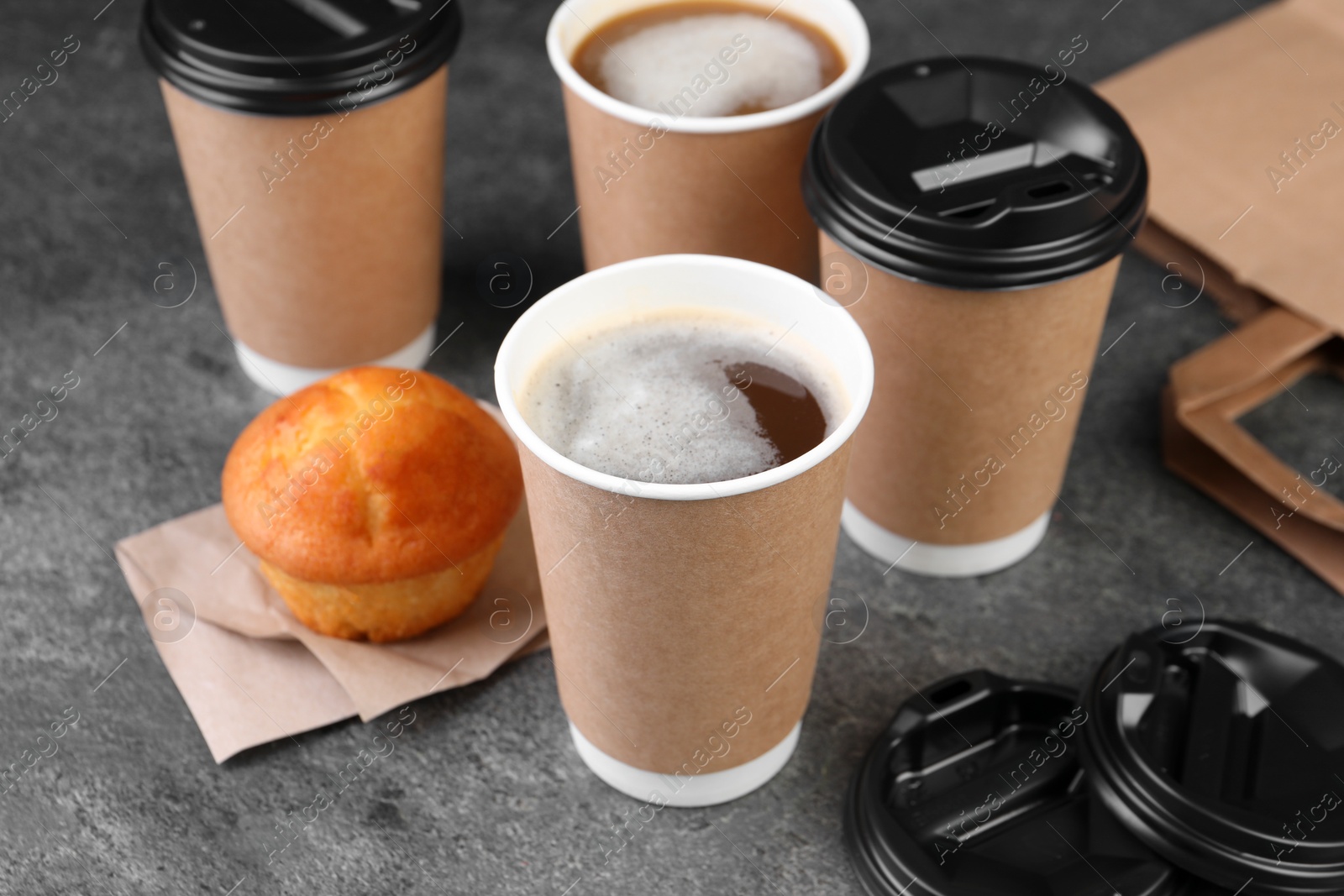 Photo of Coffee to go. Paper cups with tasty drink and muffin on grey table, closeup