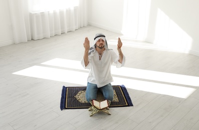 Muslim man with Koran praying on rug indoors