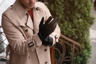 Photo of Stylish man putting on black leather gloves outdoors, closeup. Space for text